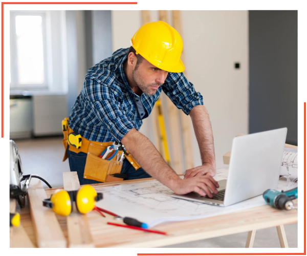 A man in construction gear working on a laptop.